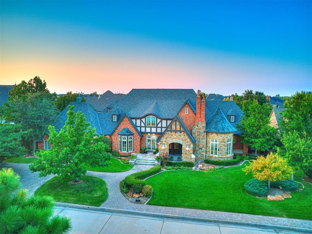 tudor-style house with a yard, curved driveway, and a chimney