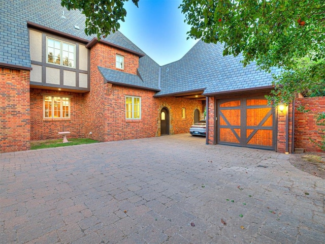 back of house featuring aphalt driveway, a garage, brick siding, stucco siding, and a high end roof