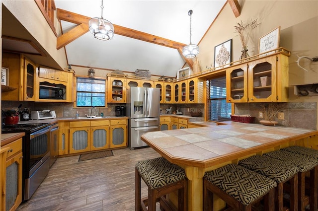 kitchen featuring stainless steel appliances, a peninsula, a sink, wood finished floors, and tile counters