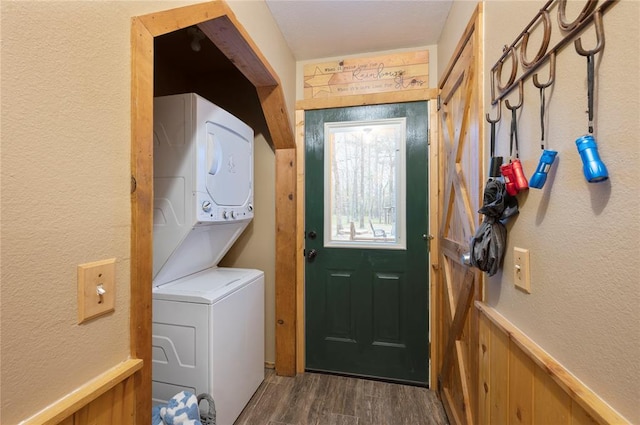 laundry room featuring a wainscoted wall, a textured wall, stacked washer / dryer, wood finished floors, and laundry area