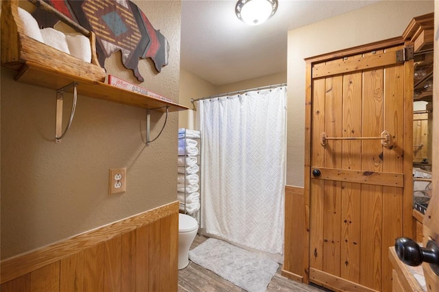 full bathroom with toilet, a shower with curtain, wood finished floors, and wainscoting