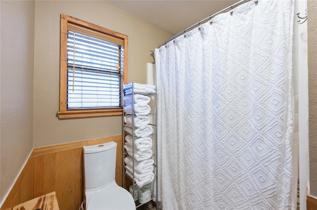 bathroom featuring a shower with shower curtain, wainscoting, and toilet