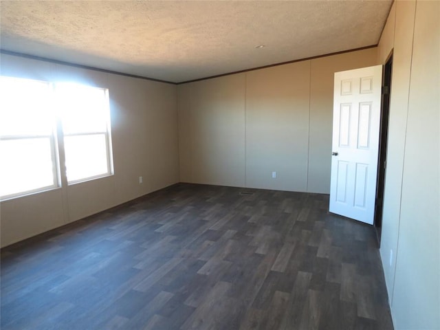 empty room with a textured ceiling, dark wood finished floors, and crown molding