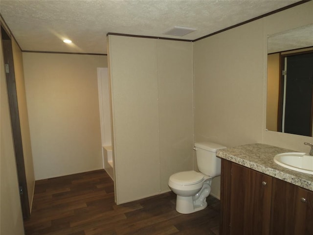 bathroom featuring toilet, vanity, wood finished floors, crown molding, and a textured ceiling