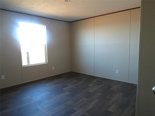 spare room with a textured ceiling, visible vents, and dark wood-style flooring