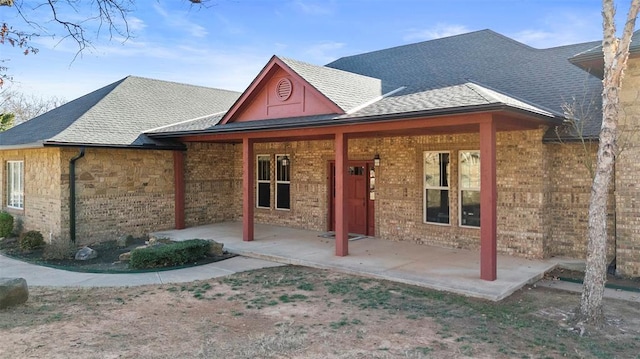 view of front facade featuring a patio area, roof with shingles, and brick siding