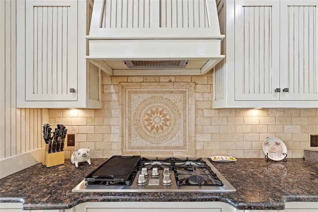 kitchen featuring tasteful backsplash, dark stone counters, custom range hood, stainless steel gas stovetop, and white cabinetry