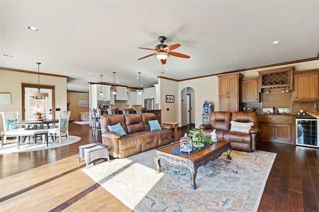 4600 Clipper Xing, Edmond, OK 73013 - living area with wine cooler, a ceiling fan, arched walkways, ornamental molding, and dark wood-type flooring