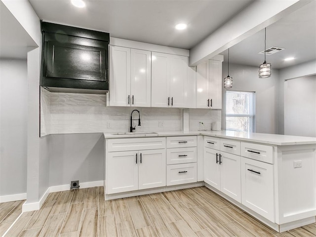 kitchen featuring a peninsula, a sink, white cabinets, and decorative backsplash