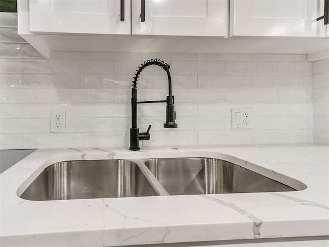 details featuring tasteful backsplash, a sink, white cabinetry, and light stone countertops