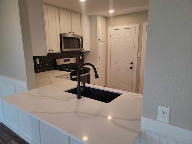 kitchen featuring tasteful backsplash, white cabinets, light stone counters, stainless steel appliances, and a sink