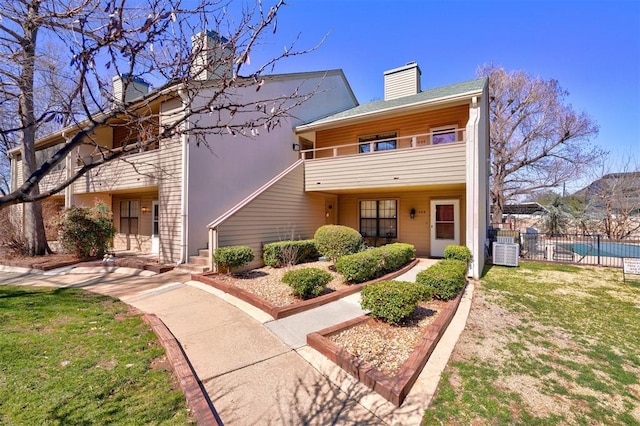 multi unit property featuring a front lawn, fence, cooling unit, a balcony, and a chimney