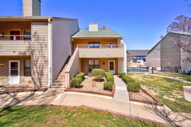 view of front facade featuring stairway, a balcony, a chimney, and fence