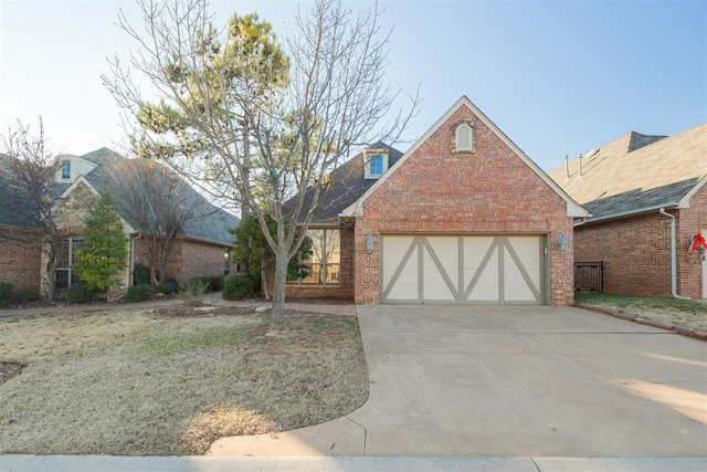 english style home featuring concrete driveway, an attached garage, and brick siding