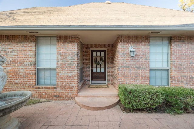 property entrance featuring brick siding and roof with shingles