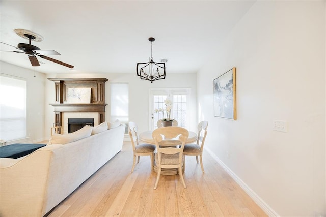 dining space featuring ceiling fan with notable chandelier, a fireplace, light wood-type flooring, and baseboards