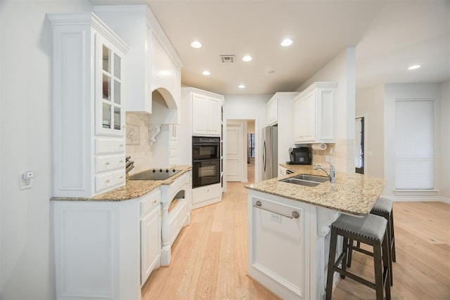 kitchen featuring visible vents, a breakfast bar, a peninsula, black appliances, and white cabinetry