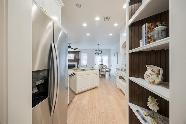 kitchen featuring visible vents, light wood finished floors, a fireplace, stainless steel appliances, and white cabinetry