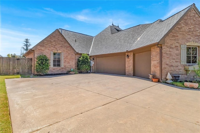 view of front of home with brick siding, a shingled roof, fence, concrete driveway, and an attached garage