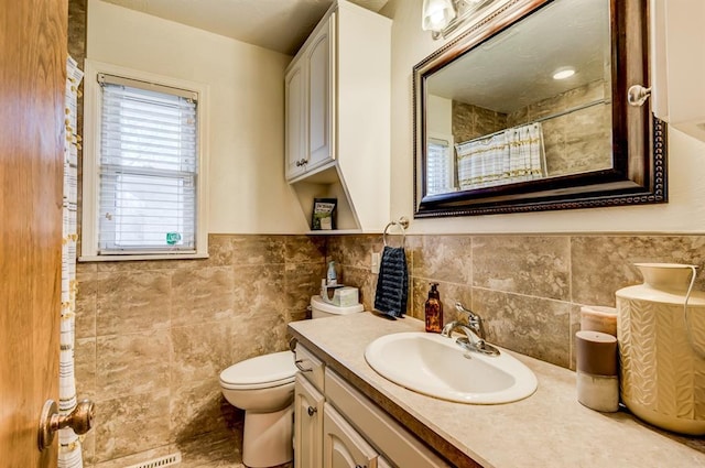 bathroom with tile walls, curtained shower, toilet, wainscoting, and vanity