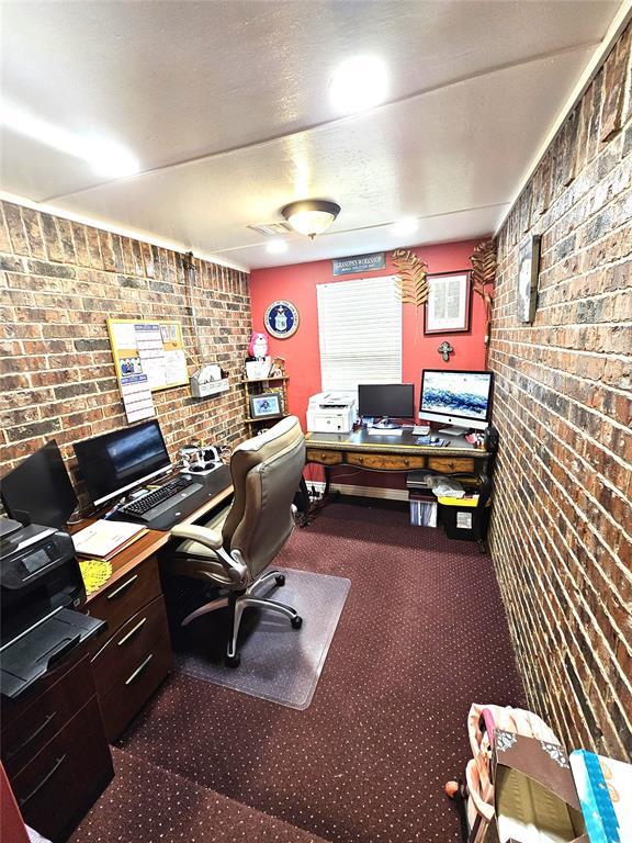 home office featuring brick wall and dark colored carpet