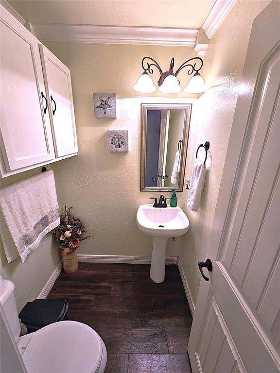 half bath featuring crown molding, a textured wall, toilet, wood finished floors, and baseboards