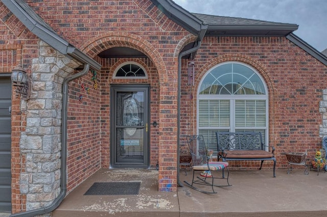 view of exterior entry with stone siding, brick siding, and roof with shingles