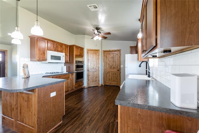 kitchen with brown cabinetry, white microwave, a peninsula, stainless steel double oven, and a sink