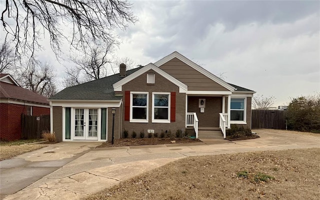 view of front of house with a chimney, covered porch, fence, french doors, and brick siding