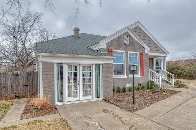 view of front of home featuring french doors, brick siding, a chimney, a shingled roof, and fence