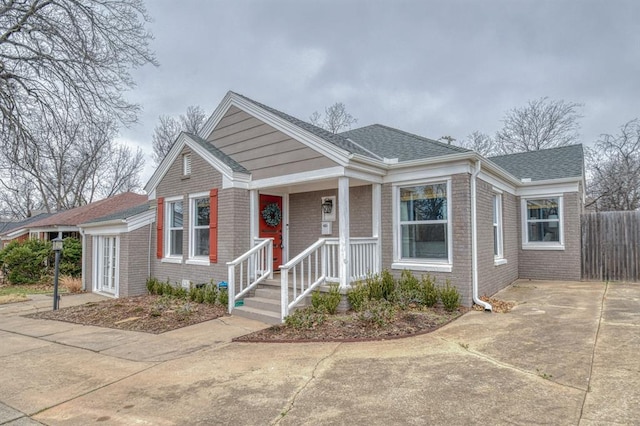 bungalow-style house with concrete driveway, brick siding, fence, and roof with shingles