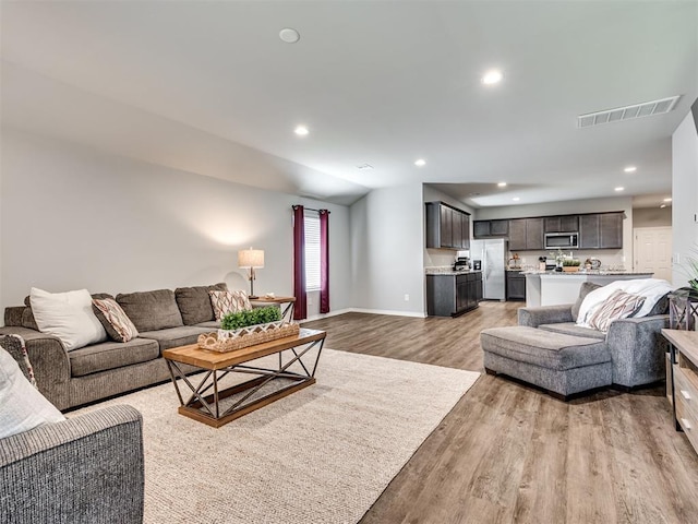 living room featuring light wood finished floors, baseboards, visible vents, vaulted ceiling, and recessed lighting