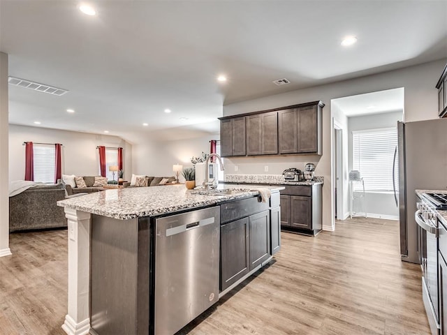 kitchen featuring stainless steel appliances, a kitchen island with sink, open floor plan, and visible vents