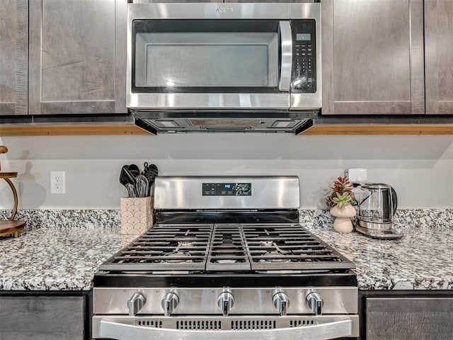 kitchen with appliances with stainless steel finishes, light stone counters, and dark brown cabinetry