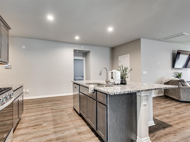 kitchen featuring light wood finished floors, stainless steel appliances, visible vents, open floor plan, and a sink