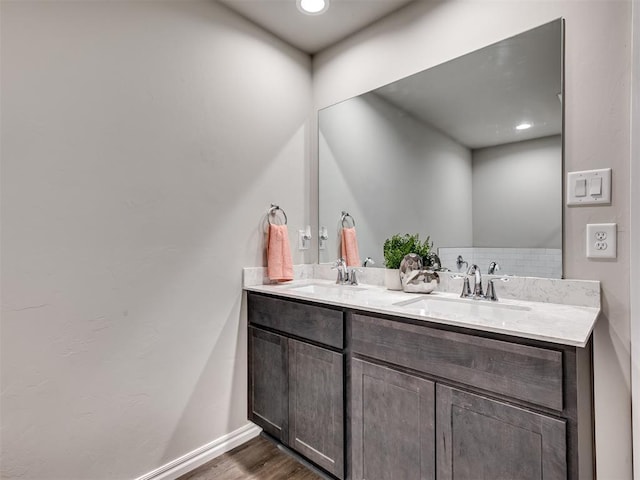 bathroom featuring double vanity, wood finished floors, a sink, and baseboards