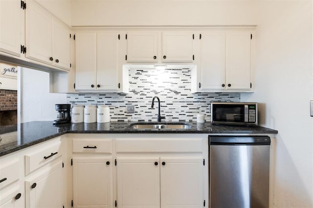 kitchen with stainless steel appliances, a sink, white cabinetry, tasteful backsplash, and dark stone countertops