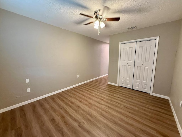 unfurnished bedroom with baseboards, visible vents, wood finished floors, a textured ceiling, and a closet