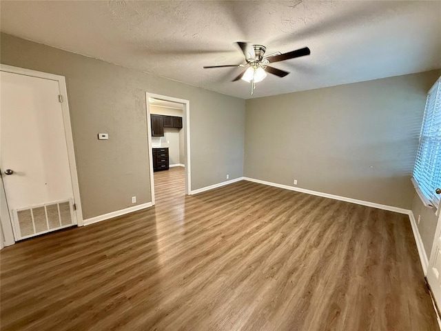 unfurnished room with ceiling fan, a textured ceiling, wood finished floors, visible vents, and baseboards