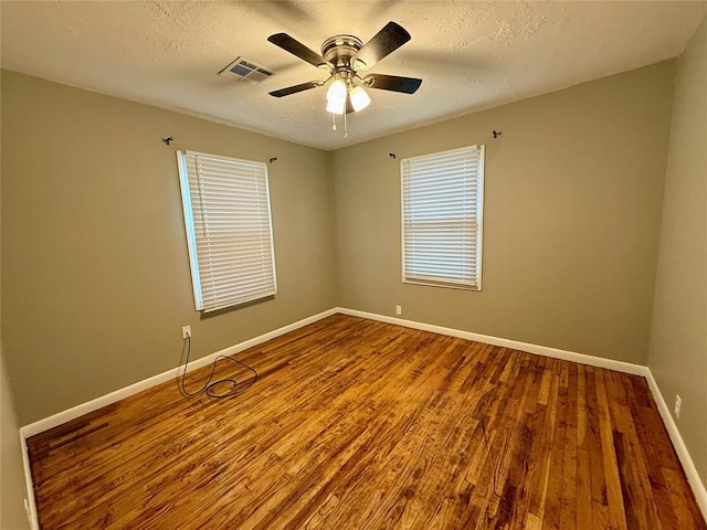 empty room with baseboards, visible vents, ceiling fan, wood finished floors, and a textured ceiling