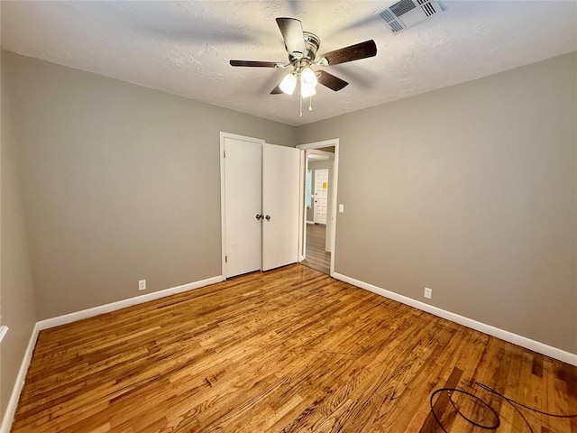 unfurnished bedroom featuring baseboards, a textured ceiling, visible vents, and wood finished floors