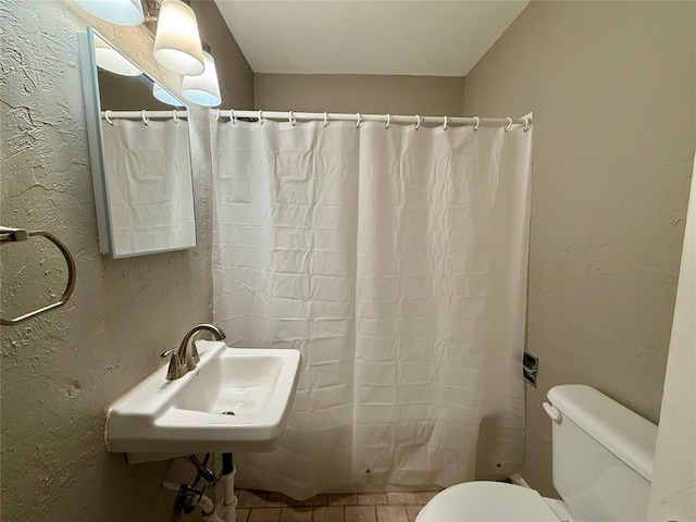 full bathroom featuring a textured wall, curtained shower, a sink, and toilet