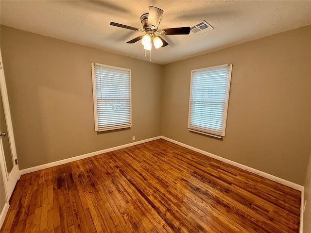 spare room featuring a wealth of natural light, visible vents, a ceiling fan, wood finished floors, and baseboards