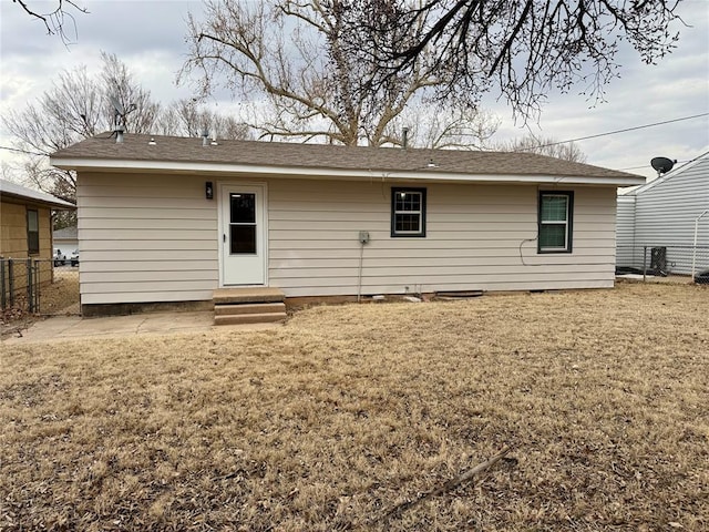 rear view of house featuring entry steps, fence, and a lawn