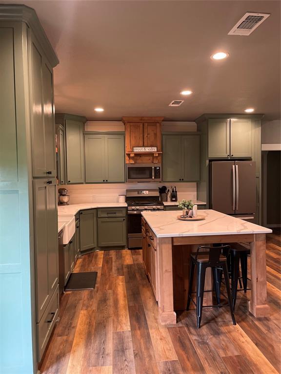 kitchen with stainless steel appliances, dark wood-style flooring, a kitchen island, visible vents, and light stone countertops