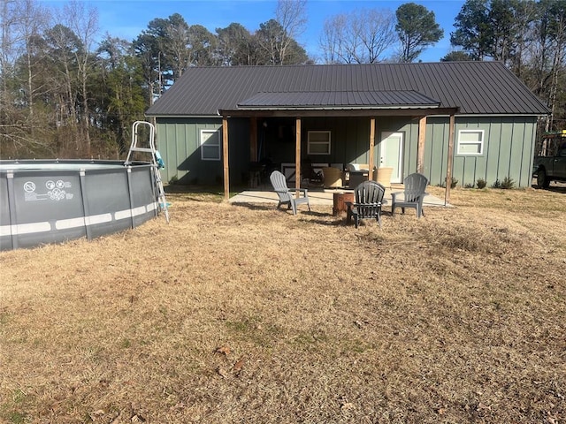 rear view of property featuring metal roof, an outdoor fire pit, an outdoor pool, and board and batten siding