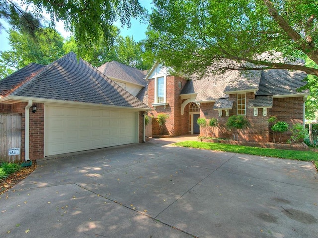 traditional-style home featuring a garage, driveway, brick siding, and a shingled roof