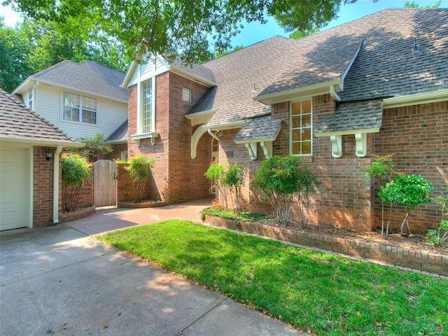 view of front of house featuring brick siding, a shingled roof, an attached garage, driveway, and a front lawn