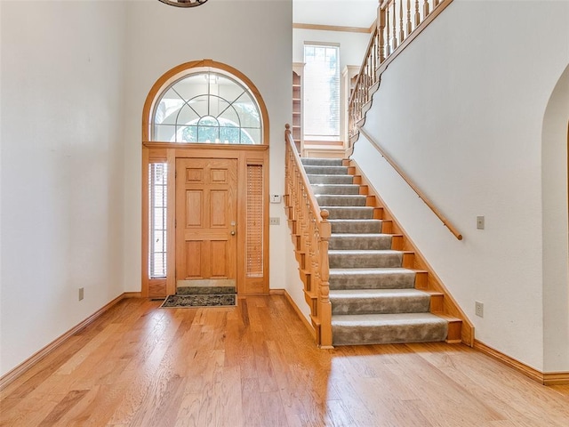 foyer entrance featuring arched walkways, a high ceiling, light wood-type flooring, and baseboards