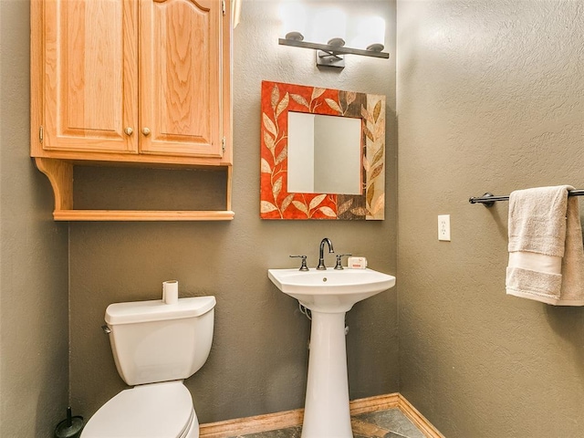 half bathroom with a textured wall, a sink, and toilet